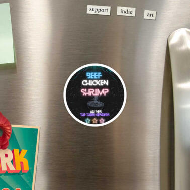 a black circle magnet on a fridge and on it, it says, "beef, chicken, shrimp ah yes the three genders." the tone is sily and the colors are the trans flag colors.